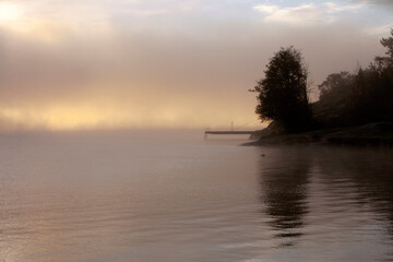 Sunrise and fog in southern Norway - silhouette of tree and small jetty with calm sea