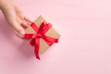 Paper gift box with red ribbon holding by hand on pink background, Present for giving in special day, Top view