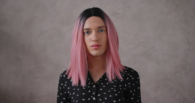 Attractive young transwoman in stylish black dot clothes with bright pink wig poses for camera on beige color background closeup