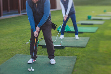 Obraz premium Group of golfers practicing and training golf swing on driving range practice, men playing on golf course, golf ball at golfing complex club resort