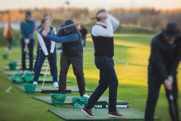 Group of golfers practicing and training golf swing on driving range practice, men playing on golf...