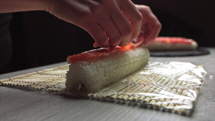 Cropped anonymous cook hands with rolling fresh sushi with bamboo mat while working in authentic Japanese restaurant,Close-up of chef's hands rolling a sushi roll on bamboo mat.Sushi making process