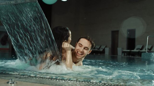 Funny couple piggybacking in spa pool. Handsome man and woman cuddling jacuzzi