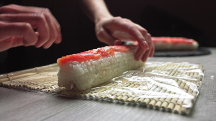 Cropped anonymous cook hands with rolling fresh sushi with bamboo mat while working in authentic Japanese restaurant,Close-up of chef's hands rolling a sushi roll on bamboo mat.Sushi making process © GRAFStock