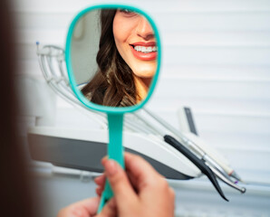 Pretty, unrecognizable woman holding mirror at dentist and smiling, perfect teeth 