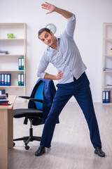 Fototapeta na wymiar Young handsome male employee doing exercises in the office
