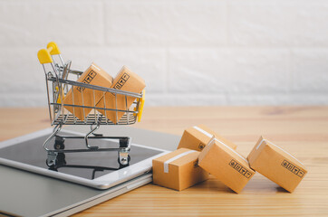 Brown paper boxs in a shopping cart with tablet on wood table in office background.Easy shopping with finger tips for consumers.Online shopping and delivery service concept.