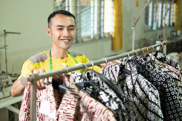 male tailor standing while tidying the clothes on the hanger rack in the garment convection production room