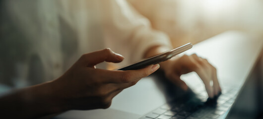 Woman hand holding smartphone with laptop on the table, for your advertisement.