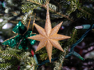 A sparkly star shaped Christmas tree ornament hanging from a pine branch

