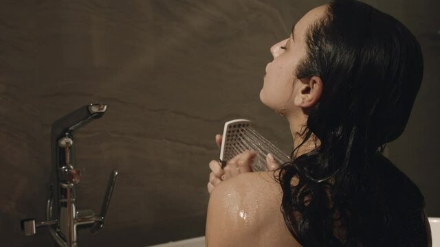 Pretty woman watering body from shower. Joyful girl relaxing in bath.