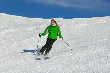 Fototapeta na wymiar Skier sliding down a snowy slope in green jacket