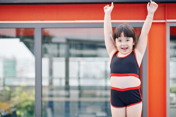Excited little Vietnamese girl in swimsuit ready to swim in pool