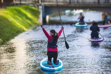 Group of sup surfers stand up paddle board, women stand up paddling together in the city river and canal - obrazy, fototapety, plakaty
