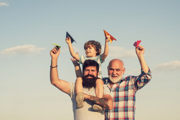 Grandfather with son and grandson having fun in park. Happy child playing with toy paper airplane against summer sky background. Child happy. Enjoy family together.