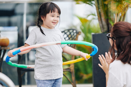 Mother clapping to her little daughter playing with hula hoop outdoors