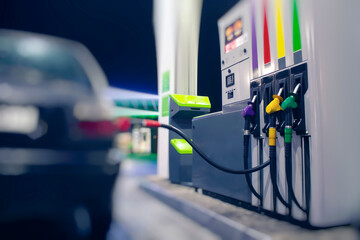 A gas hose is installed in a car at a night gas station with a store in the background and bright lights.