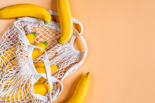 Top view of ripe bananas and white mesh shopping bag with copyspace on orange pastel bagground