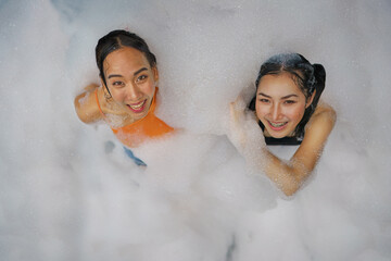 asian women friends enjoy playing together in foam bobbles pool party