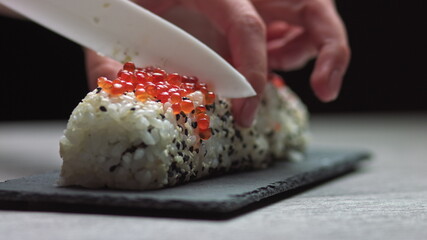 Chef cutting rolls of sushi with a knife on a stone board. - shot at a low angle. Beautiful female hands cut sushi.