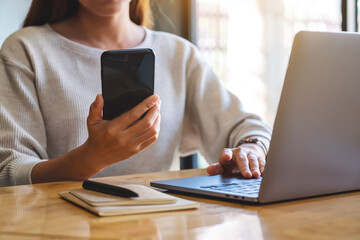 Closeup image of a woman holding and using mobile phone and laptop computer in office