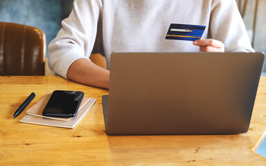 Closeup image of a woman holding credit cards while using laptop computer in office