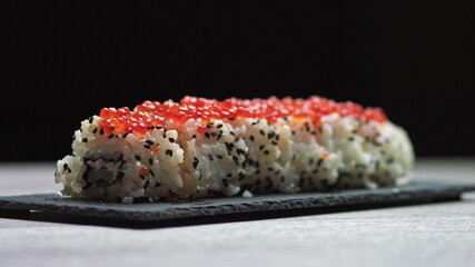 Sticks Take Sushi from Sushi box. Variety of types sushi with red caviar, fish, Philadelphia cheese and chopsticks close-up. Set of delicious Japanese sushi rolls.sushi on a stone board on a black