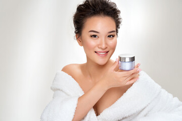 Obraz na płótnie Canvas Woman holds jar with cosmetic cream. Photo of asian woman after shower on white background. Beauty and skin care concept