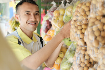 Shop assistant arranging hanging plastic fruit packaging in a fruits shop