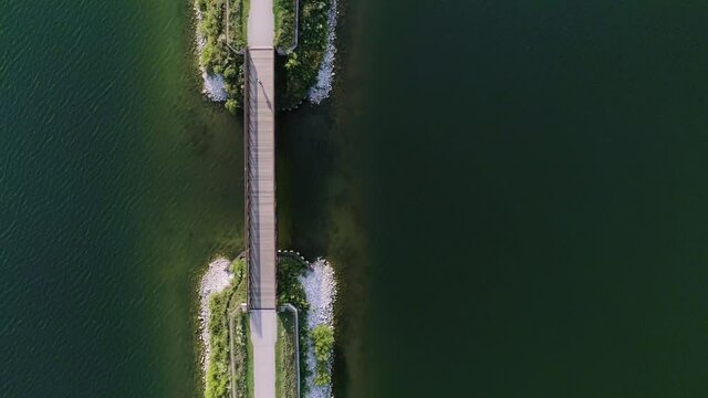 Offset aerial shot of woman running across a small bridge spanning a lake.