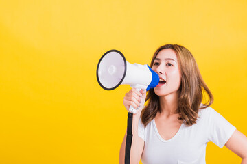 Fototapeta na wymiar Asian Thai happy portrait beautiful cute young woman stand to make announcement message shouting screaming in megaphone looking to side away, studio shot isolated on yellow background with copy space