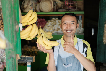 young man smiling with fresh fruit bananas in fruits shop with thumbs up