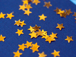 Gold star glitter confetti splashed on blue paper background.