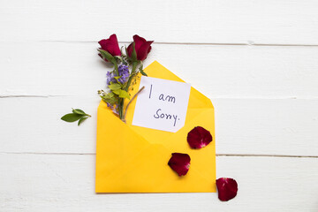 i am sorry message care handwriting with red rose flowers in yellow envelope arrangement flat lay...