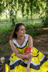 Young beautiful girl in a yellow dress with a book in the park. Reads, studies, rest