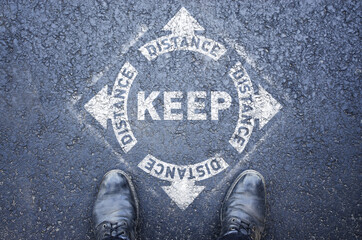 Man standing on white sign. keep distance. Sign painted on the pavement reminding users to maintain a physical distance during the COVID-19 pandemic.