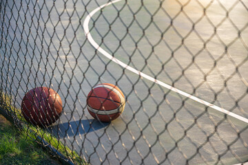 Basketball ball on illuminated playground at night with metal net on foregound