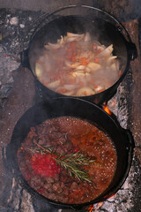 two cast iron pots with game goulash on the campfire, dutch oven, outdoor cooking