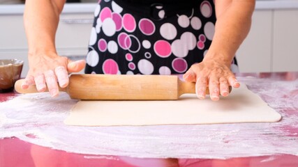 female hands roll out the dough with a rolling pin on a wooden surface, close-up. female hands...