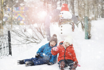 Children in the park in winter. Kids play with snow on the playground. They sculpt snowmen and slide down the hills.