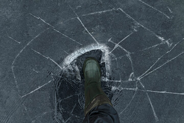 Fisherman foot on broken cracked thin ice at lake. Dangerous winter fishing