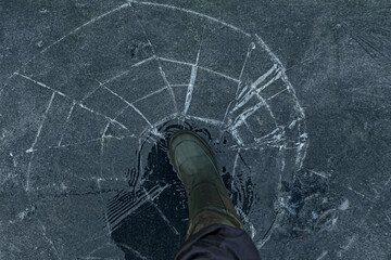 Fisherman foot on broken cracked thin ice at lake. Dangerous winter fishing