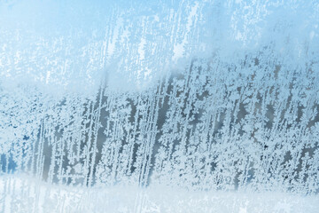 View of the coniferous forest through the frozen window with frosty patterns.
