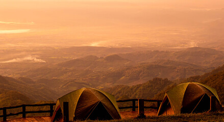 Fototapeta premium Two tents stands against the background of beautiful mountain landscape with the warm sunset light.
