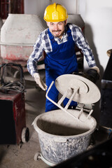 Young smiling man using concrete mixer for construction work at workshop.