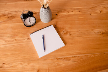 Black alarm clock, notepad and stationary on a wooden table. Deadline and education concept. Top horizontal view copyspace.
