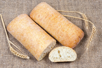 Partly cut and whole ciabatta, wheat ears on a burlap