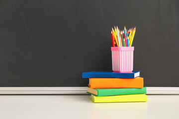Holder with pencils and books on table in classroom