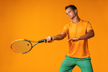 Studio shot of a young tennis player holding racket against orange background