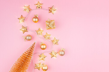 Golden christmas decorations with christmas tree, glowing stars garland on soft light pink background, copy space, top view.